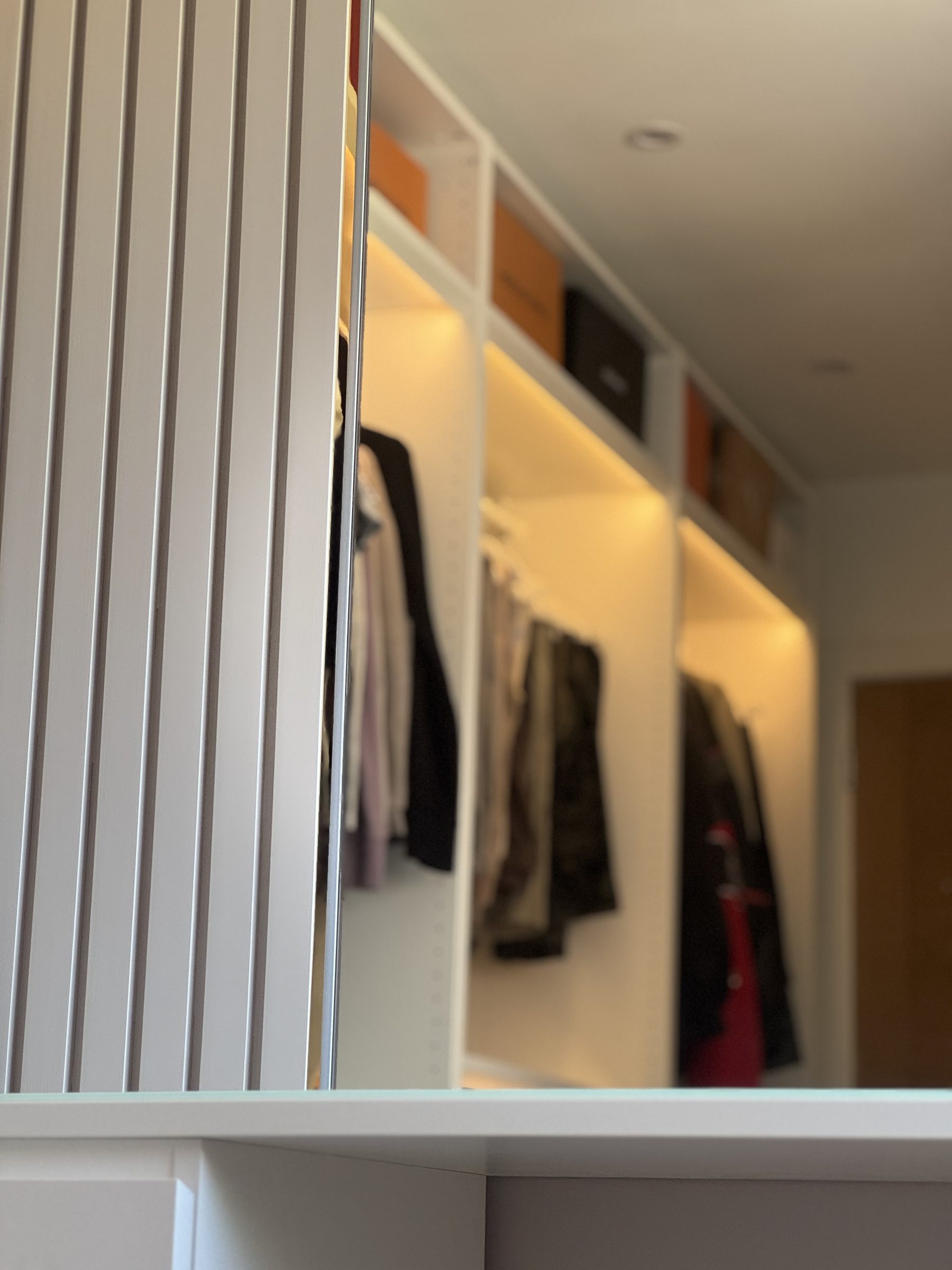 Fitted wardrobe with lit interior shelving and hanging space, made by VIP Walls
